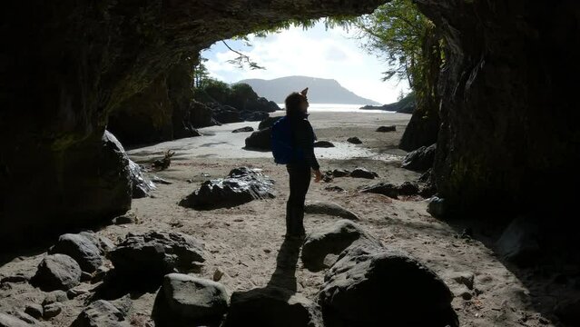 Woman Walking on in Cave on Beach with Pacific Ocean Coast View. Sunny Sky. San Josef Bay, Cape Scott Provincial Park, Northern Vancouver Island, BC, Canada. Canadian Nature Background. Cinematic 4k
