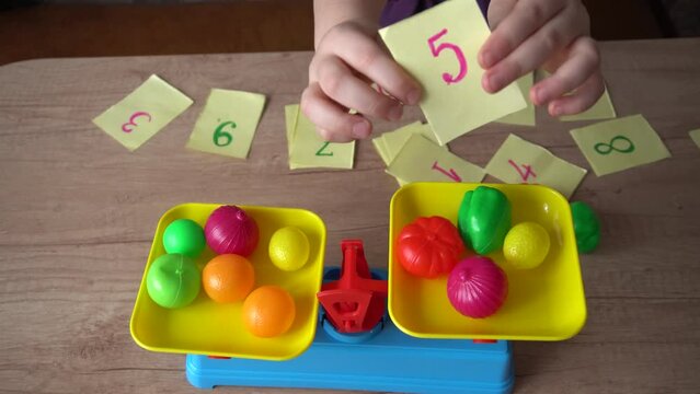 little girl plays in the store, weighs vegetables on a toy scale, and studies the numbers, close-up, the concept of children's home learning games