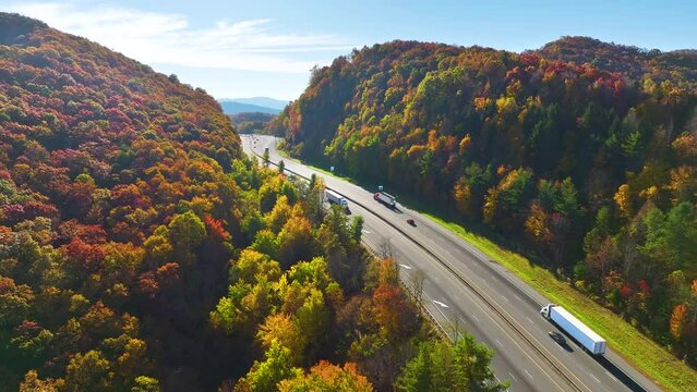 Aerial view of I-40 freeway in North Carolina heading to Asheville through Appalachian mountains in golden fall with moving trucks and cars. Interstate transportation concept