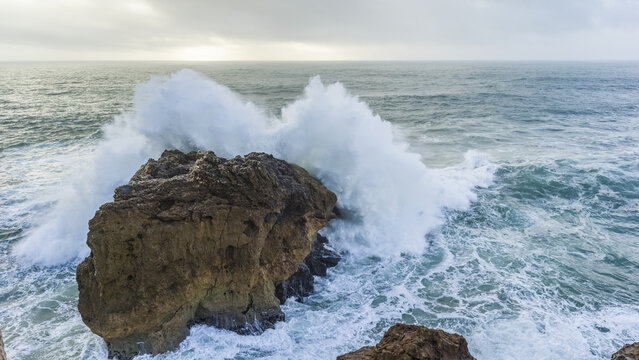 Large wave crashing into a rock along a coast. The biggest waves in the world are here in Nazare; Nazare, Leiria District, Portugal