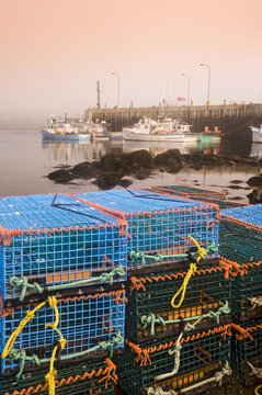 Stacked lobster traps along shoreline with boats tied up at a wharf in the background, Bay of Fundy; Tiverton, Long Island, Nova Scotia, Canada