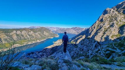 Man with panoramic view from the Ladder of Kotor on the Kotor bay during sunrise, Adriatic Mediterranean Sea, Montenegro, Balkan Peninsula, Europe. Winding fjord water reflection along coastal towns