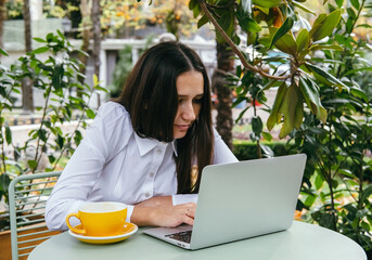 Young woman works with laptop on terrace of  cafe. Hunched posture, professional spinal deformity...