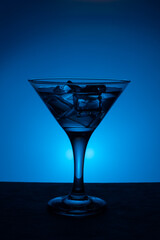 Alcoholic or non-alcoholic cocktail with ice cubes, on a blue gradient background, vertical frame