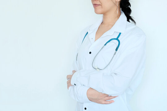 Image of confident female doctor wearing glasses, trainee with stethoscope and medical gown, arms crossed like a professional looking at camera confidently, against white background, Asian appearance 