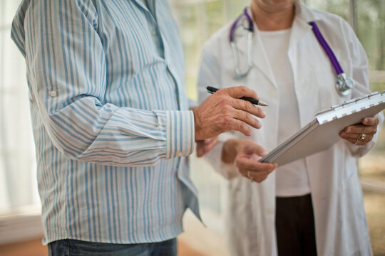 Hands of a female doctor holding a clipboard next to a male colleague holding a pen