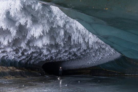 A man with a headlamp explores a Castner Glacier ice cave with hoarfrost covering the ceiling; Alaska, United States of America