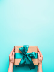 Female hands hold big gift box on turquoise blue background, copy space. Caucasian girl hands...
