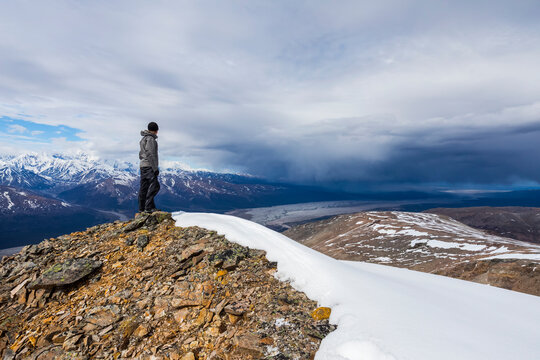 A hiker observes approaching storm clouds from a ridge in the Alaska Range; Alaska, United States of America