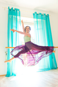 A female dancer leaps in mid-air in a dance move wearing a tulle skirt and looking at the camera; Lugano, Ticino, Switzerland