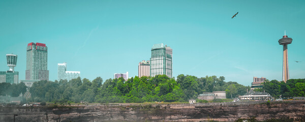 Niagara Falls Summer Travel Landscape Series, view of Canadian Side Skyline, tower, and flying birds from America Falls in New York, USA, retro-style photography in turquoise-tone