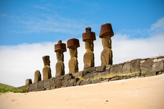 A sandy slope leads the eye towards a platform and a row of five moais seen from behind, Anakena beach; Easter Island, Chile