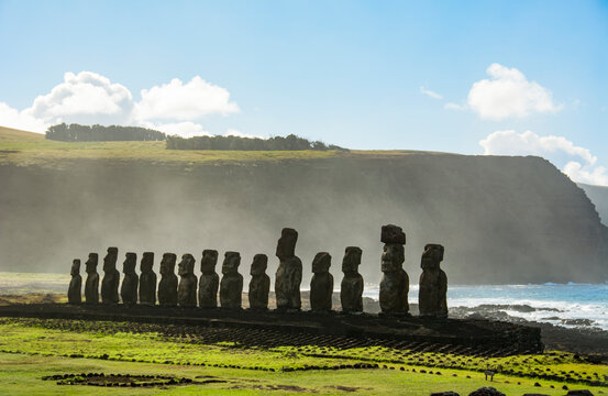The fifteen moais of Tongariki seen from afar in decreasing perspective against the ocean and blue sky; Easter Island, Chile