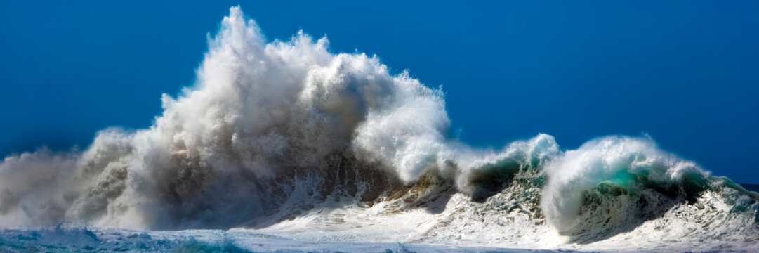 Large wave breaking off the Na Pali coast against a bright, blue sky; Kauai, Hawaii, United States of America