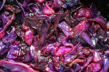 Red cabbage are pan-fried until lightly charred, then braised in mulled wine. Background of fry blue cabbage in a section, macro. Closeup, top view. Texture and pattern of purple cabbage
