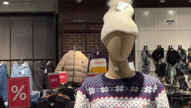 Male mannequin in a reindeer sweater and a knitted hat stands in the window of a clothing store