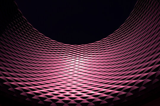 Low angle view of a patterned outdoor building facade reflecting pink light and black background, Messe Basel Exhibition Centre; Basel, Basel Stadt, Switzerland
