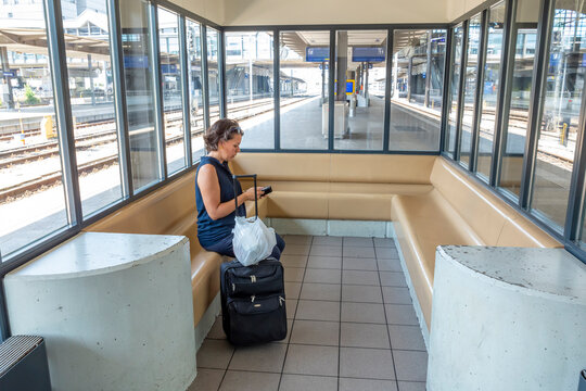 Female passenger using her smart phone while waiting for train with suitcase in Basel SBB railway station; Basel, Basel Stadt, Switzerland