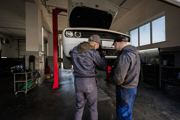 Two mechanic in service repair station calibrate the distronic in muscle car in lift.