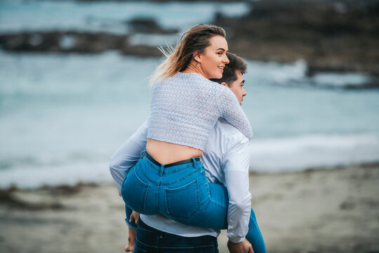 A young couple at the beach, the young woman being carried on the young man's back; Wellington, North Island, New Zealand