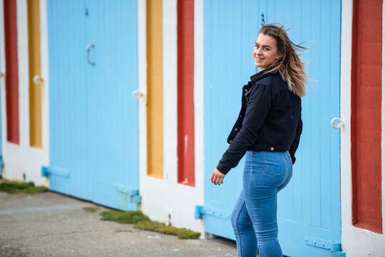 A Young Woman Walks Down The Street Along A Colourful Building, Looking Back Over Her Shoulder At The Camera; Wellington, North Island, New Zealand