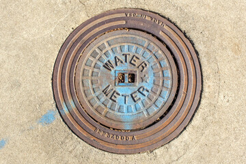 Circular Metal Water Meter sign in a sidewalk.
