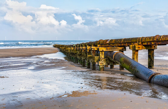 Pipe carrying waste to the North Sea at Cambois Beach with wind turbines in the distance; Northumberland, England