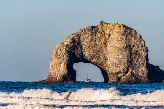 A fishing boat is framed by a stone arch at Rockaway Beach; Rockaway, Oregon, United States of America
