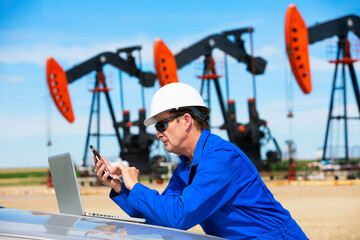 Man working on a laptop and smart phone with pumpjacks in the background; Alberta, Canada