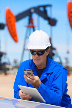 Man working on a tablet and smart phone with pumpjacks in the background; Alberta, Canada