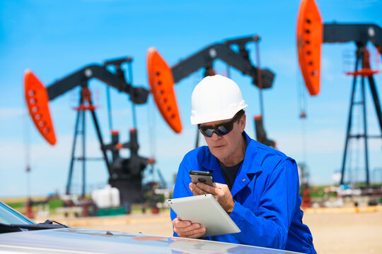 Man working on a tablet and smart phone with pumpjacks in the background; Alberta, Canada