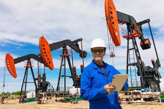 Man working on a tablet with pumpjacks in the background; Alberta, Canada
