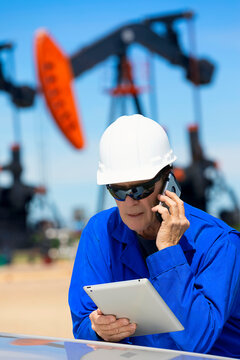 Man working on a tablet and smart phone with pumpjacks in the background; Alberta, Canada
