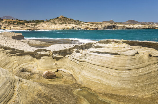 Eroded rock formations along the shore and turquoise ocean water along the coast of a greek island; Milos, Greece