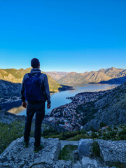 Man with panoramic view from the Ladder of Kotor on the Kotor bay during sunrise, Adriatic Mediterranean Sea, Montenegro, Balkan Peninsula, Europe. Winding fjord water reflection along coastal towns