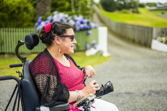 Maori woman with Cerebral Palsy in a wheelchair going down a sidewalk; Wellington, New Zealand