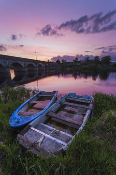 Two old wooden boats on the banks of the Shannon River at sunset with a stone bridge in the background; Montpellier, County Limerick, Ireland