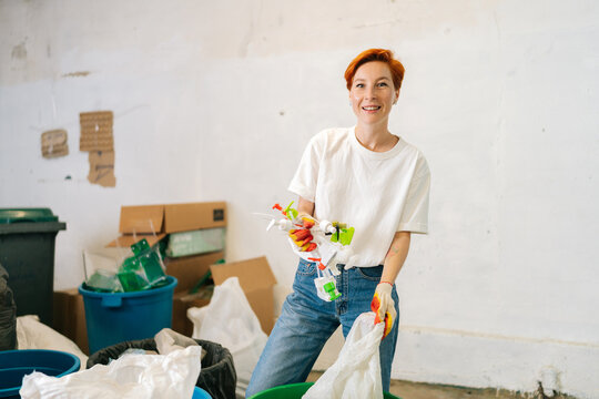 Portrait of smiling female worker wearing latex gloves sorting diverse plastic waste for further disposal at modern private waste recycling plant. Concept of environment protection and zero waste