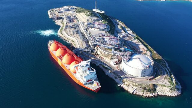 Aerial drone top down video of LNG (Liquified Natural Gas) tanker anchored in small gas terminal island with tanks for storage to store and regasify LNG