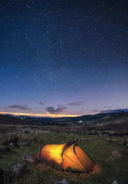 A lit up tent pitched in the Wicklow Mountains at night with stars in the sky; County Wicklow, Ireland