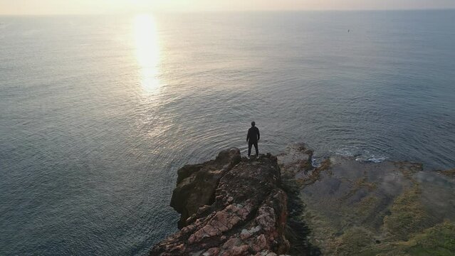 A young man stands on a cliff by the sea and looks thoughtfully ahead.