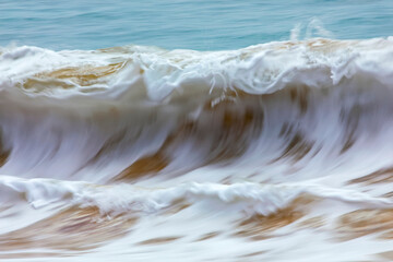 Motion blur of foamy rolling waves carrying golden sand at the shore; Kihei, Maui, Hawaii, United States of America