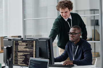 Two young colleagues discussing new program codes on computer during work in modern office