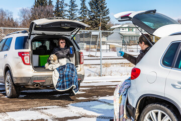 Two women sit in the back of their vehicles in a parking lot to visit during the Covid-19 world pandemic; St. Albert, Alberta, Canada