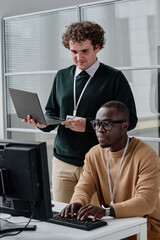 African American developer typing codes on keyboard with his colleague standing in background and...