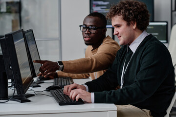 Programmer pointing at computer monitor with codes and talking to his colleague while they working...