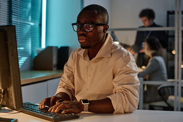 African American programmer concentrating on his online work on computer working in office till...