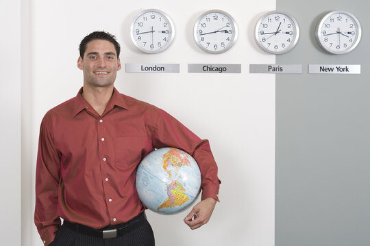 Businessman Holding Globe Standing by Clocks Showing International Time Zones