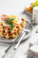 Cheese or potato savory waffles served with tomatoes, cream cheese, ham and bazil leaves with cutlery and linen napkin close up. Delisious savory breakfast
