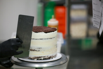 Decorator using spatula and scraper smoothing buttercream frosted layered tall cake - obrazy, fototapety, plakaty